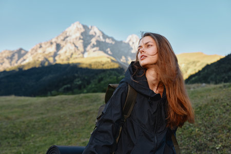 A solo hiker woman stands outdoors in a mountainous landscape. She carries a backpack and gazes...