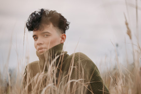 A close portrait of a young person in tall grass wearing a warm sweater, conveying authentic...