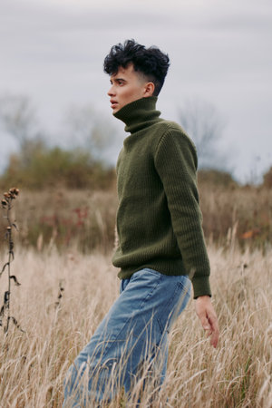 Young man in a knit turtleneck walks through tall dry grass, captured in a candid portrait...