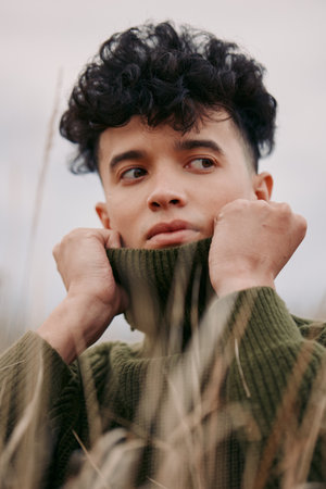 A candid portrait of a young person outdoors in a chunky knit sweater, conveying authenticity...