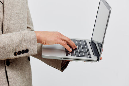Professional woman in beige blazer typing on a silver laptop with white background, business...