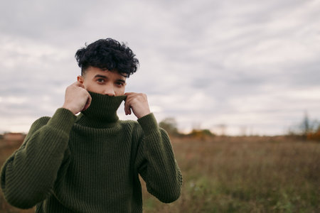 Young man in a textured green sweater pulls the collar up, revealing a sincere expression and...