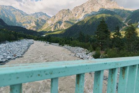A scenic mountain landscape featuring a rocky river, evergreen trees, and a railing in the...