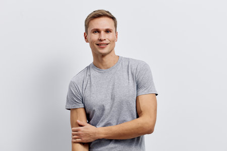 Smiling young man with short light brown hair wearing casual grey t-shirt looking at camera pose isolated on plain light grey background studio portrait. People lifestyle conceptの写真素材