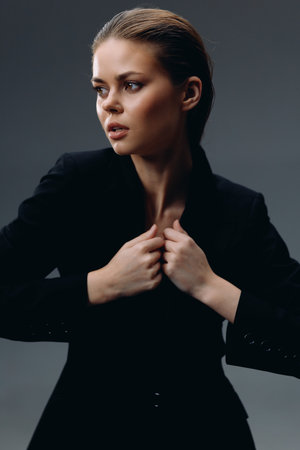 Portrait of a thoughtful woman in black suit with slicked-back hair and neutral expression in dark studio lighting.の写真素材