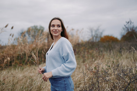 A candid portrait of a woman standing in a windswept field, conveying authenticity and quiet confidence. Natural light captures an honest expression and textured knitwear detail.の写真素材