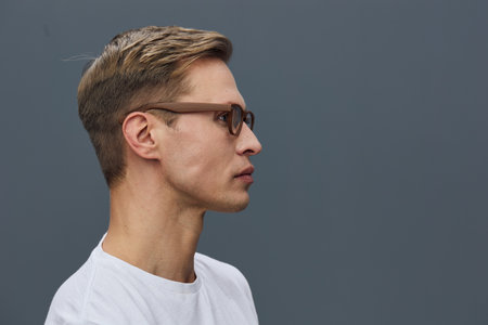 Stylish young man with brown hair and glasses in profile view, wearing a white t-shirt, posing...