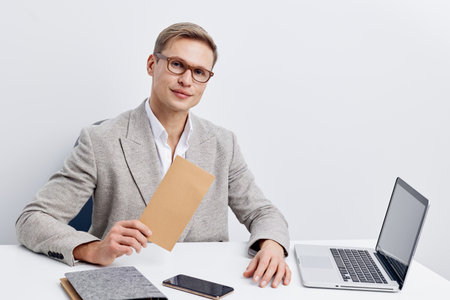 Professional young man with glasses in formal blazer sitting at desk with laptop and folders in...