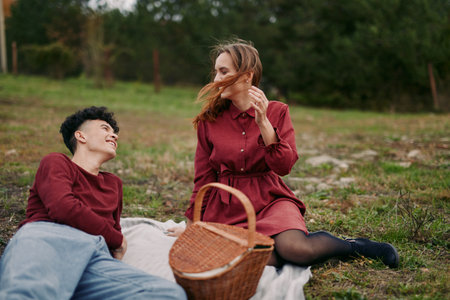 Young couple relaxing on a picnic blanket in a grassy meadow, sharing a candid moment with genuine smiles and natural interaction that conveys authenticity, quiet reliability and heartfelt connection.の写真素材