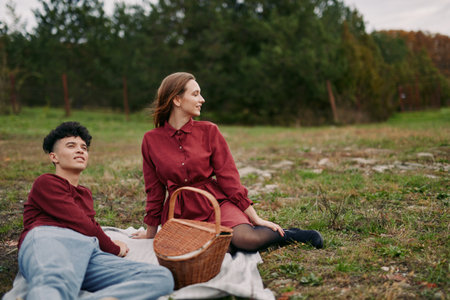 A candid outdoor portrait of a young couple relaxing on a picnic blanket, warm natural interaction and authenticity in their expressions conveying reliability and honest everyday connection in nature.の写真素材
