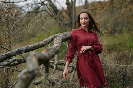 Portrait of a woman in a red dress standing beside a weathered branch, conveying authentic mood and natural pose in a calm rural landscape.の写真素材