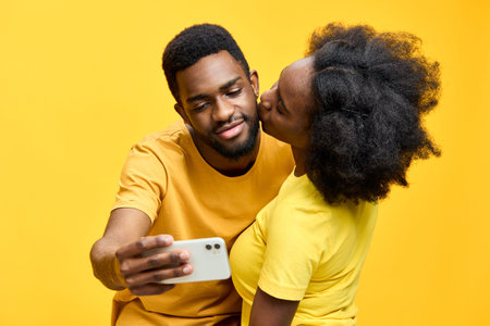 Happy couple taking a selfie together in matching yellow outfits against a bright yellow background, celebrating love and joyの写真素材