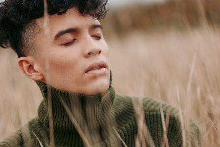 A serene portrait of a young person outdoors, eyes closed, skin lit warm, wearing a green knit...