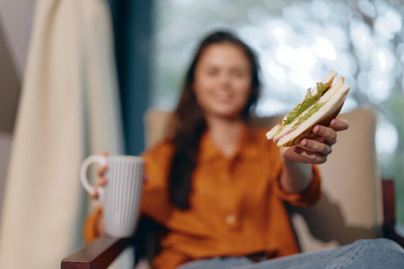 Cheerful young woman enjoying a healthy sandwich and coffee in a cozy indoor setting, radiating...