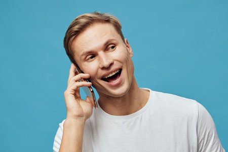 Smiling man talking on mobile phone, cheerful expression, casual white t-shirt, natural light,...