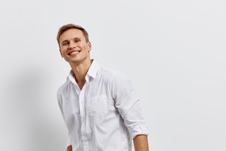 Smiling young man with light brown hair wearing a white shirt looks joyful against a plain white background. Studio portrait capturing happiness, positive attitude, casual style, and approachable demeanor.の写真素材