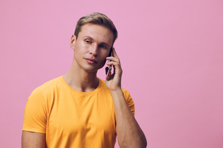 thoughtful man talking smartphone wearing orange t-shirt look side pink background digital communication conceptの写真素材