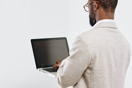 Professional man with glasses in beige blazer working on a laptop isolated on plain white background, close-up of back view. Modern technology, workplace, business concept, serious mood, office environment.の写真素材