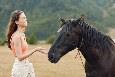 A cheerful woman stands in an open field, reaching out to a horse. She smiles warmly, creating a calm, friendly moment and a gentle connection with nature.の写真素材