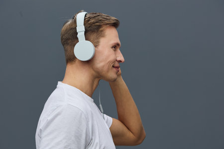 Close-up of a young man wearing white headphones on a plain gray background studio portrait,...