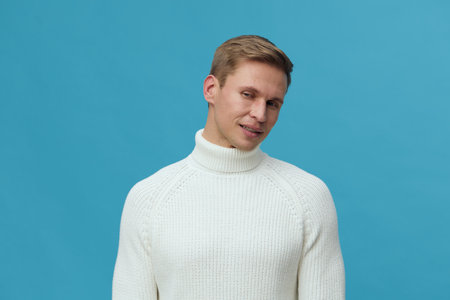 Man in white knitted turtleneck sweater looking down smile blue background digital detox mental health conceptの写真素材