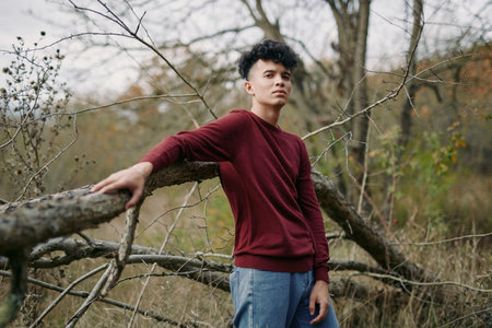 A candid portrait of a young man leaning on a weathered fence in an autumn field, expressing authenticity and credibility through posture, light, and quiet realism.の写真素材