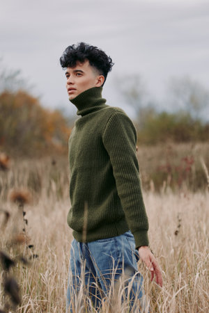 A calm portrait of a man in a green knit turtleneck standing in field grass, conveying authenticity...