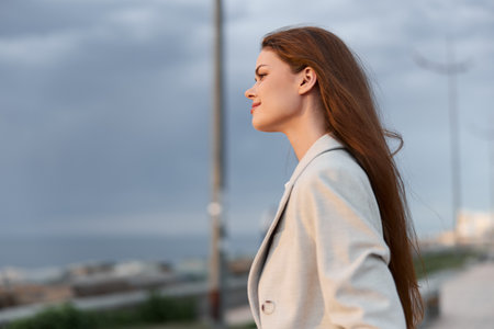 Confident woman in light blazer standing outdoors with calm expression during cloudy day, modern business portrait, natural light, serene moodの写真素材