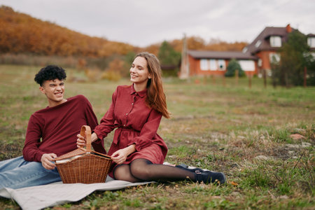 Young couple enjoying a picnic in the countryside, candid expressions and natural poses conveying authenticity and accuracy of a relaxed autumn outing with a wicker basket on a blanket.の写真素材