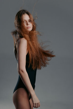 Young woman with long flowing hair wearing black bodysuit against grey backgroundの写真素材