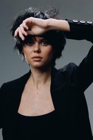 young woman with short black hair posing with hand near face wearing black blazer and dark topの写真素材