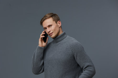 Smiling man talking on mobile phone, wearing cozy gray turtleneck sweater, modern casual style,...