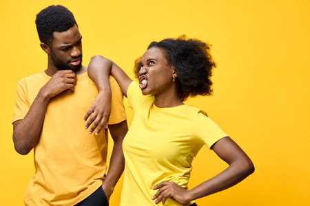 African American couple expressing playful disagreement in matching yellow shirts against a vibrant yellow background, showcasing emotions of frustration and humorの写真素材