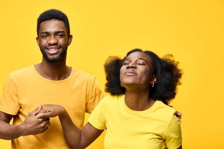 Joyful young African couple in matching yellow outfits, expressing love and happiness against a bright yellow background, perfect for seasonal celebrationsの写真素材