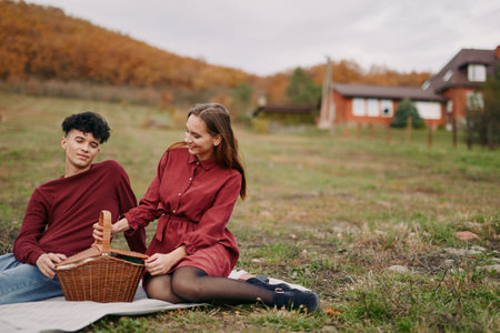 A candid outdoor picnic portrait of a young couple sharing a quiet moment on a blanket, conveying natural emotions, authenticity and veracity in everyday rural leisure and personal connection.の写真素材