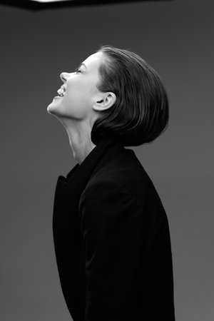 Smiling woman in black coat, black and white portrait with joyful expression and elegant style.の写真素材