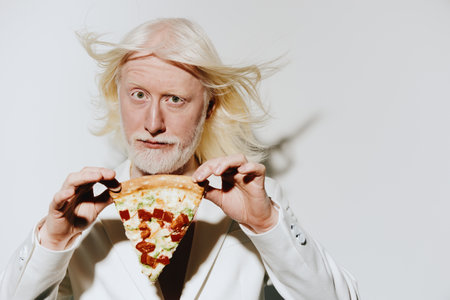 Man with white hair holding a slice of pizza against a white background, showcasing a playful and whimsical concept with an emphasis on food enjoyment and expressionsの写真素材
