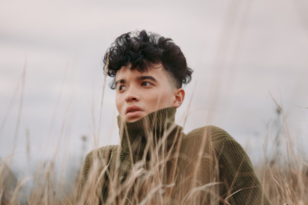 Close-up portrait of a young person in tall grass, captured with a natural, authentic expression and realistic tones, emphasizing genuine emotion and an unposed documentary style.の写真素材