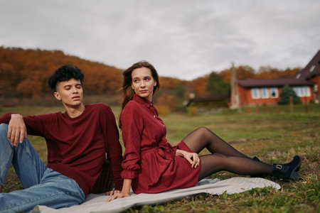 A candid outdoor portrait of a young couple relaxing on a blanket in autumn countryside, portraying an authentic, credible connection and believable emotion in a natural, unposed moment.の写真素材