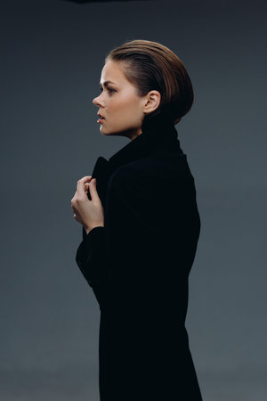 Profile of a young woman wearing a black coat with a serious expression on a dark background.の写真素材