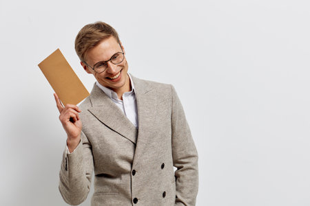 smiling man wearing beige suit jacket holding envelope isolated on white background positive emotions concept digital nomad mail communicationの写真素材