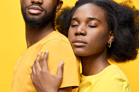 Young black couple embracing with closed eyes, wearing matching yellow shirts against a vibrant yellow background, exuding love and warmthの写真素材