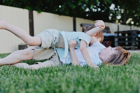 Two playful boys wrestle on a lush green lawn, showcasing joyful moments of childhood and camaraderie, radiating fun and energy in a sunny setting.の写真素材