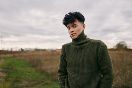 Young man in a thick green turtleneck stands in an open field, captured as a natural, unposed portrait that highlights real moments and a believable, true-to-life presence. (159 characters)の写真素材
