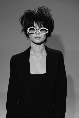 Stylish woman wearing black suit and white sunglasses with short messy hair in black and white portrait.の写真素材