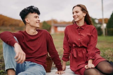 Young couple sit on a picnic blanket in an autumn park, sharing a candid smile and natural connection that highlights authenticity and credibility in a relaxed everyday moment.の写真素材