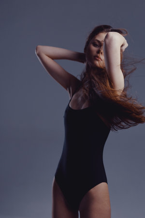 elegant woman in black bodysuit posing with closed eyes against gray background in studio lightingの写真素材