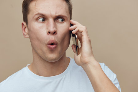 Confused man talking on phone with surprised expression, looking aside against plain neutral...