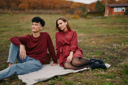 Candid portrait of a young couple sharing a relaxed countryside picnic, natural expressions and genuine connection captured in warm autumn light, conveying a truthful, lived moment.の写真素材