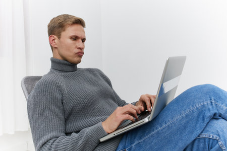 Man working on laptop computer while sitting on a couch in a modern minimalistic room, casual...